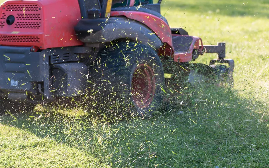 A red zero-turn mower cutting grass, clippings spraying out from under the deck