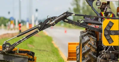 A tractor-mounted boom mower trimming grass along a roadside verge